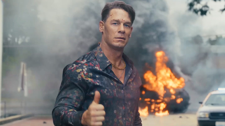 Chris Smith (John Cena) donne un coup de pouce avec une explosion derrière lui dans une rue de la ville de la saison 2 de la pacificateur 2