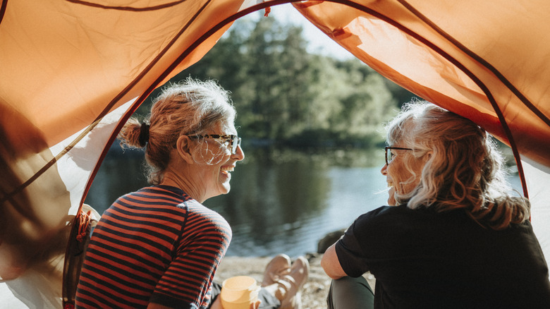 Deux femmes âgées souriant dans une tente par un lac