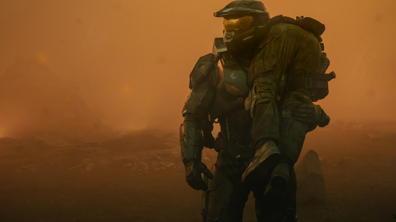 Pablo Schreiber en tant que maître chef portant un soldat blessé sur son épaule dans un paysage rempli de brume orange à Halo