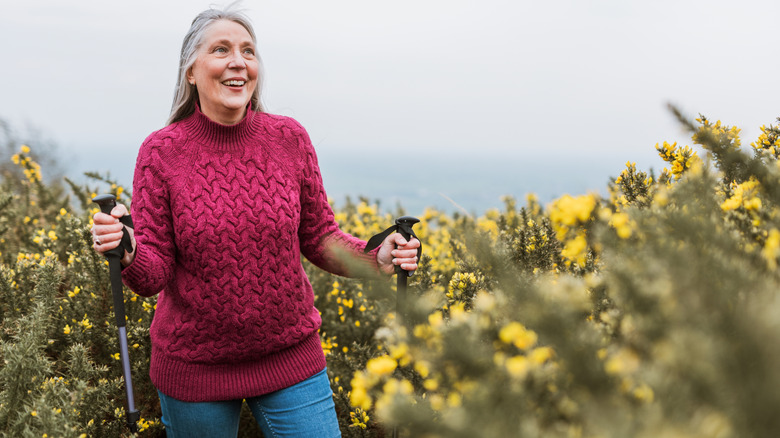 Femme senior en randonnée dans la nature, souriant dans un pull rose.