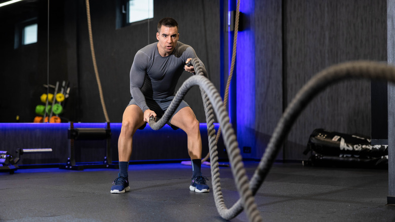 Un homme fort se concentrant sur l'amélioration de son ton musculaire grâce à des exercices de corde de bataille focalisés dans un espace d'entraînement innovant adapté à des performances d'entraînement optimales.