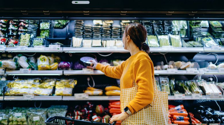 Jeune femme asiatique avec panier, portant un sac à provisions réutilisable, achetant des fruits et légumes biologiques frais au supermarché.