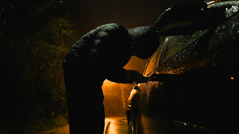 Un homme avec un capot essayant de pénétrer dans une voiture.
