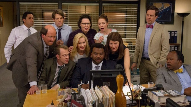Les employés de Dunder Mifflin se sont rassemblés autour d'un ordinateur sur "Le bureau"