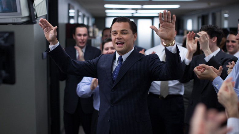 Leonardo DiCaprio comme Jordan Belfort portant un costume et levant ses mains devant une foule enthousiaste dans le loup de Wall Street