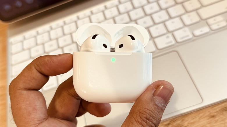 main gauche tenant AirPods 4 avec couvercle de cas ouvert