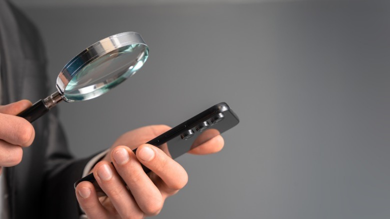 Personne inspecter un téléphone avec une loupe