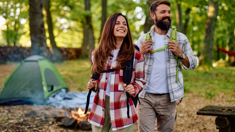 Des randonneurs souriants avec des sacs à dos se promènent dans une forêt luxuriante, profitant de leur aventure en plein air près d'un camping confortable