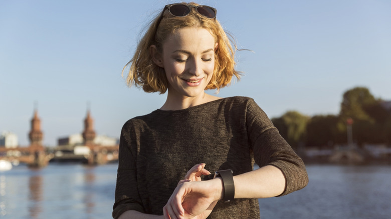 Une femme aux cheveux courts et aux lunettes de soleil sur sa tête vérifie sa montre.