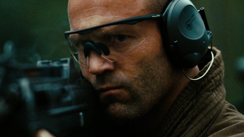 Jason Statham comme Arthur Bishop portant des écouteurs tout en tirant un pistolet dans le mécanicien
