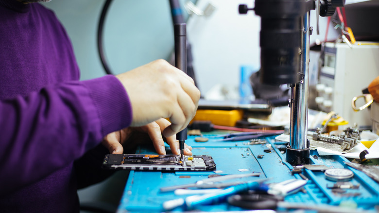 Technicien démêlant le smartphone avec tournevis.