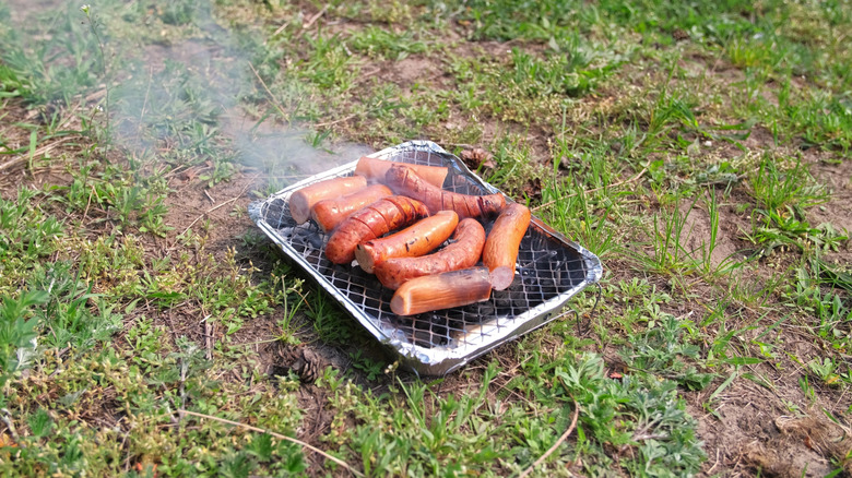 Saucisses cuisinées sur le gril à charbon jetable sur l'herbe