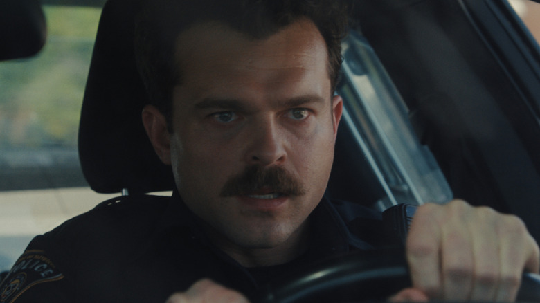 Alden Ehrenreich en tant qu'officier Paul au volant d'une voiture de police avec une expression sérieuse sur son visage dans les armes