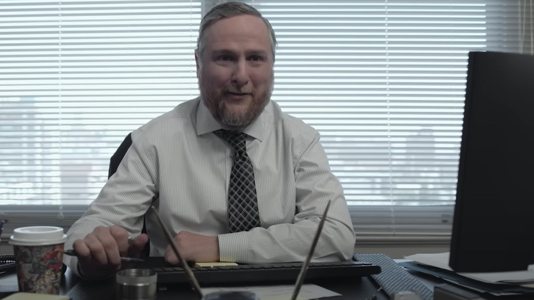 Tim Key comme Ken Davies assis à son bureau sur le papier