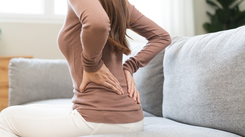 Une femme assise sur le canapé en tenant le bas du dos