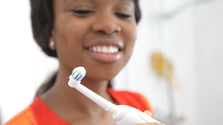 Femme afro-américaine souriante regardant la brosse à dents électrique