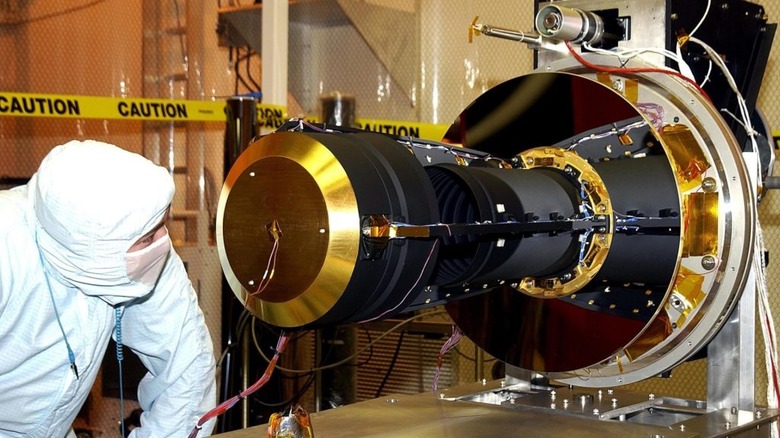 un scientifique en tenue de protection inspecte l'extrémité dorée du satellite