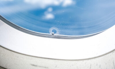 The bleed hole of a plane window is seen in closeup with a blue sky visible through the window pane