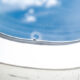 The bleed hole of a plane window is seen in closeup with a blue sky visible through the window pane