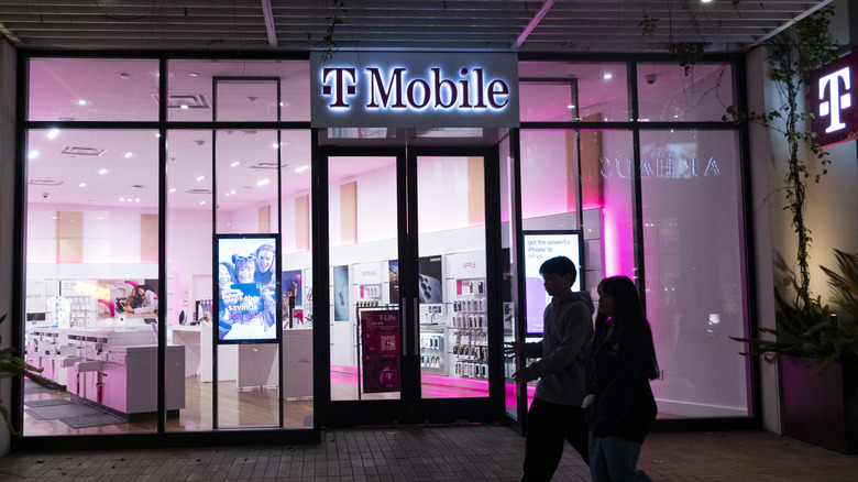 Clients devant un magasin trottoir T-Mobile avec éclairage intérieur rose