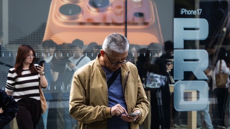 Un homme utilise son smartphone devant un Apple Store