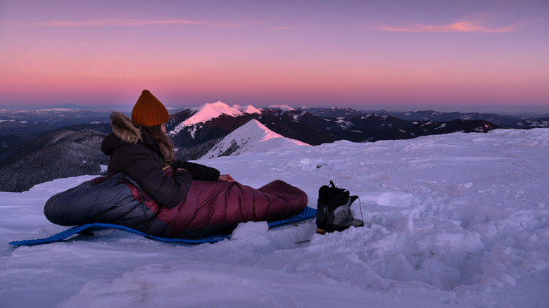 randonneuse dans un sac de couchage au coucher du soleil, sol enneigé