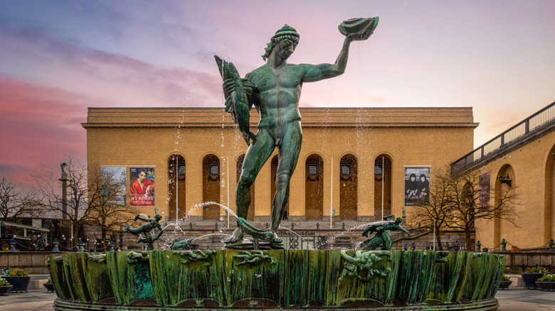 entrée du bâtiment voûté, statue verte avec fontaine, personnes