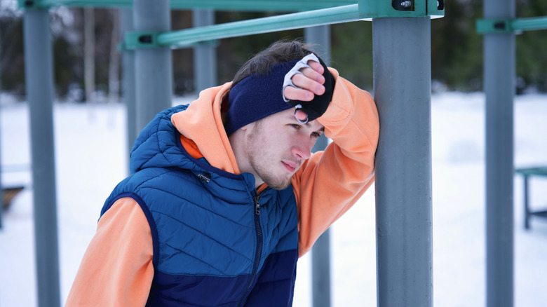 Jeune homme appuyé contre un poteau de gym dans la jungle, dans un terrain couvert de neige