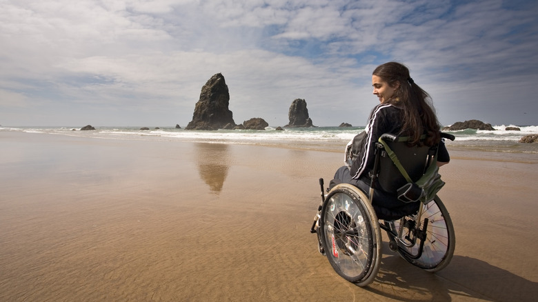Une femme en fauteuil roulant sourit sur une plage