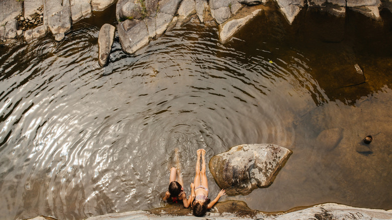 Un décor naturel mettant en scène deux adolescentes nageant dans un ruisseau clair bordé d'un terrain rocheux