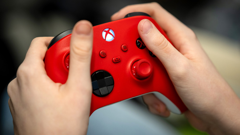 Une personne utilisant une manette Xbox rouge avec des boutons noirs, un D-pad noir et des sticks analogiques rouges
