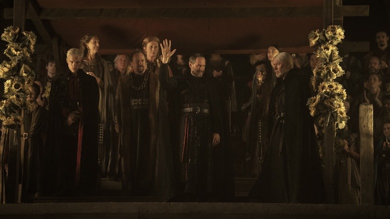 Finn Bennett dans le rôle d'Aerion, Bertie Carvel dans le rôle de Baelor et Sam Spruell dans le rôle de Maekar Targaryen debout sur un podium avec d'autres membres de la famille royale dans Un Chevalier des Sept Royaumes