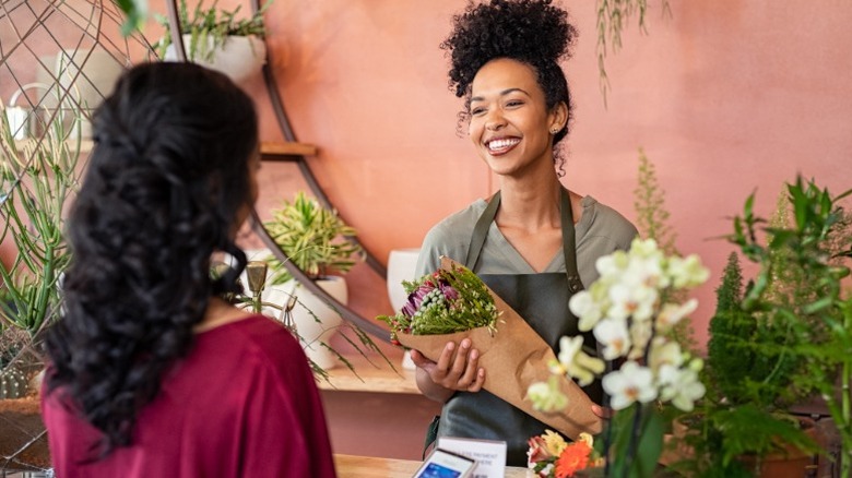 Une femme achète des fleurs à un fleuriste souriant