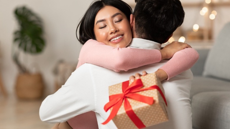 Une femme tient un cadeau tout en embrassant un homme