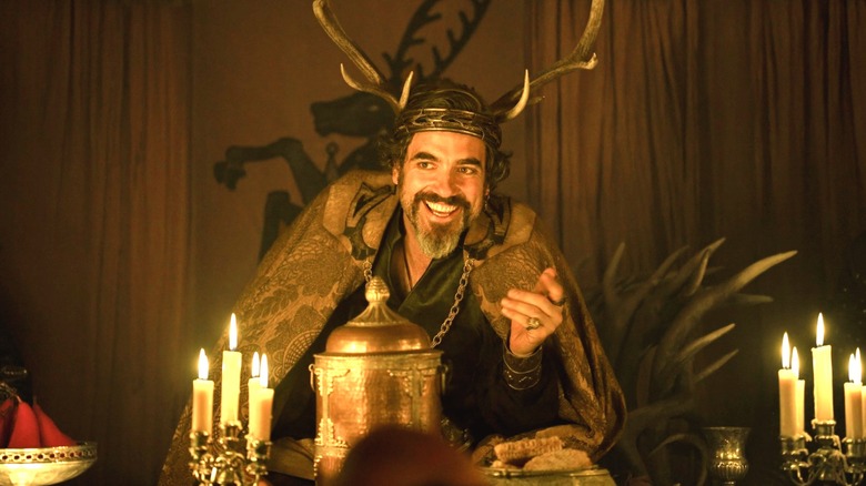 Daniel Ings dans le rôle de Lyonel Baratheon portant une couronne en bois de cerf et assis à une table éclairée par des bougies dans Un Chevalier des Sept Royaumes