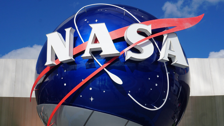 Logo de la NASA sur un globe métallique bleu à l'extérieur avec un ciel bleu en arrière-plan.
