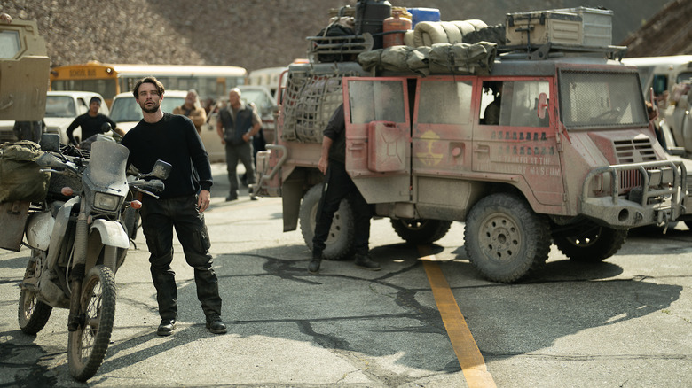 Thomas Doherty dans le rôle de Link parmi un groupe d'adeptes et de véhicules poussiéreux dans la saison 2 de Paradise