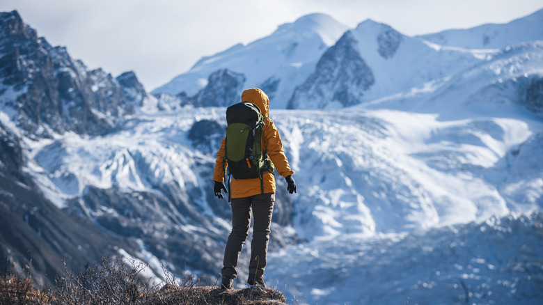Une personne portant un équipement d'hiver et un sac à dos regarde par-dessus une falaise vers des montagnes glacées.