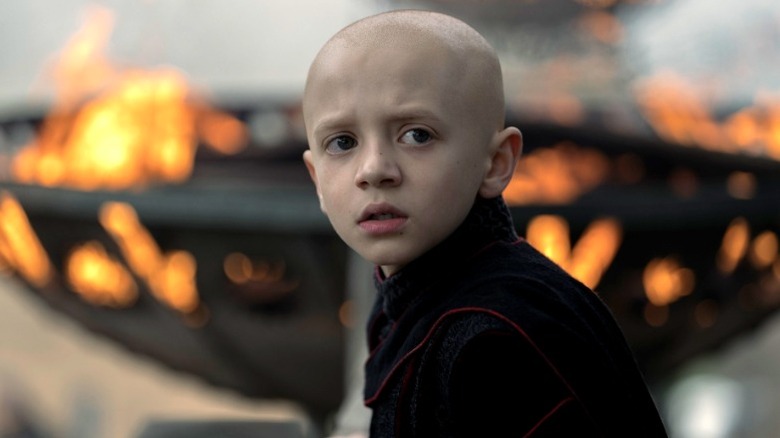 Dexter Sol Ansell dans le rôle d'Egg vêtu de noir et debout devant un brasero rempli de flammes dans Le Chevalier des Sept Royaumes