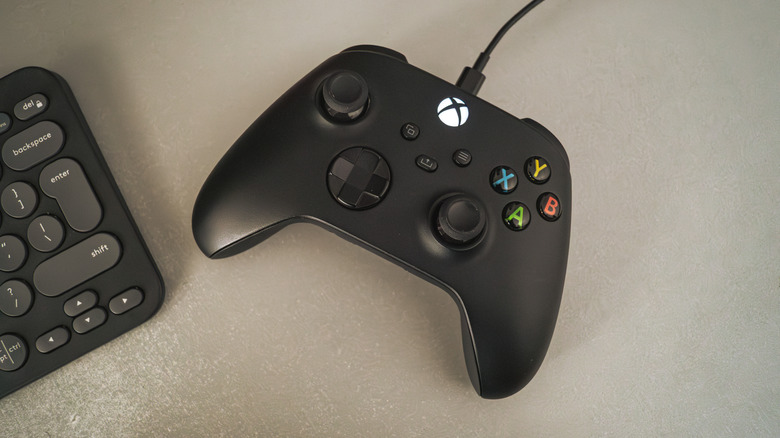 Une manette Xbox noire avec le câble branché sur un bureau gris clair, le clavier Logitech MX Pebble légèrement hors écran