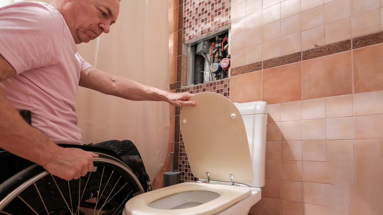 homme en fauteuil roulant abaissant le couvercle de la cuvette des toilettes