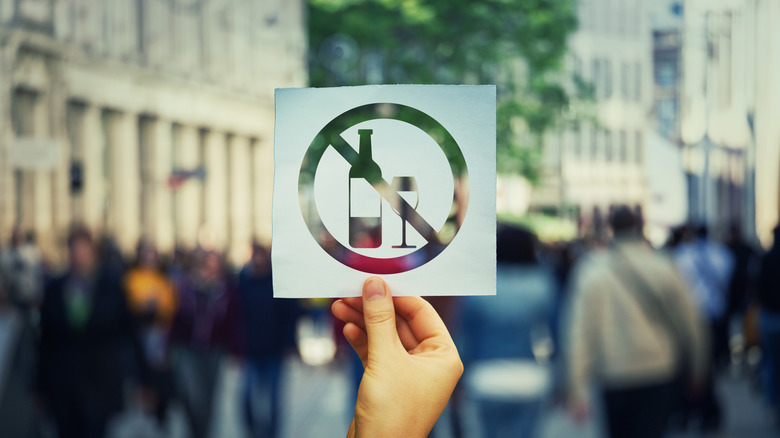 Une main tenant une feuille de papier sans signe d'alcool sur un fond de rue bondé.