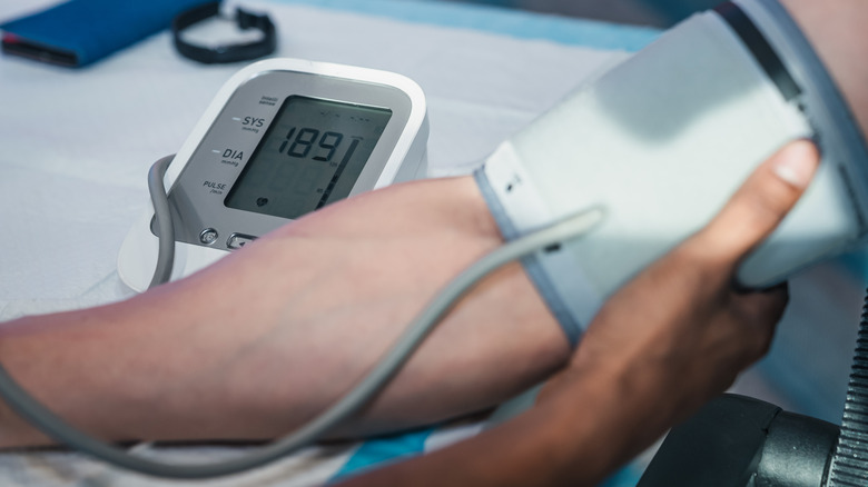 Gros plan d'un tensiomètre avec un bras enveloppé dans un brassard de tension artérielle flou au premier plan.