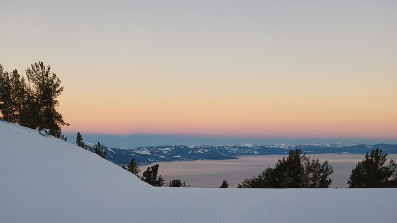 Lever du soleil sur une station de ski paradisiaque avec le lac Tahoe au loin sur une piste damée.