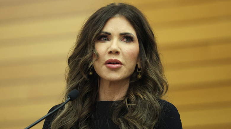 Kristi Noem portant une tenue noire et des bijoux de luxe prononce un discours lors de la cérémonie de prise de commandement