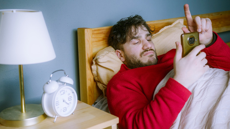Un homme allongé dans son lit en faisant défiler son téléphone.