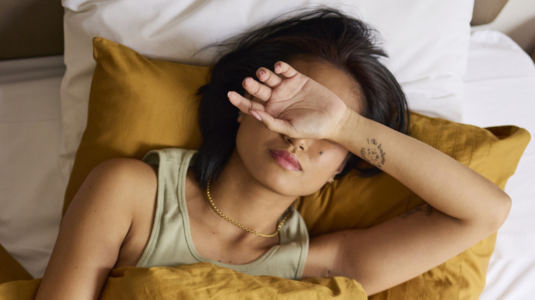 Femme avec bras sur les yeux, allongée dans son lit