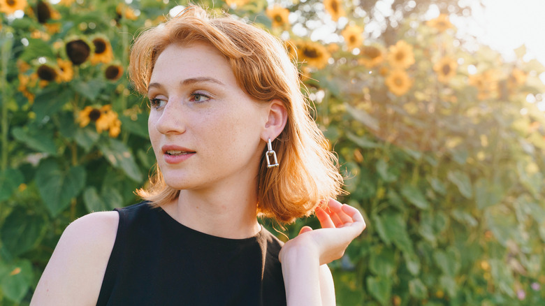 Une femme rousse regardant sur le côté devant des tournesols.