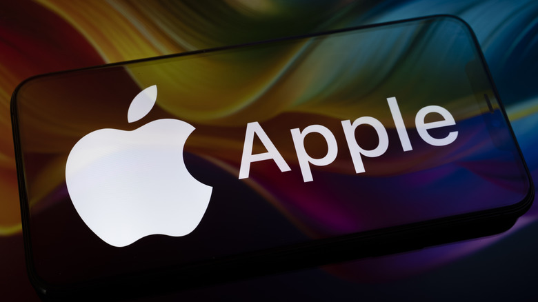 Le logo Apple apparaît sur l'écran d'un smartphone posé sur une surface réfléchissante