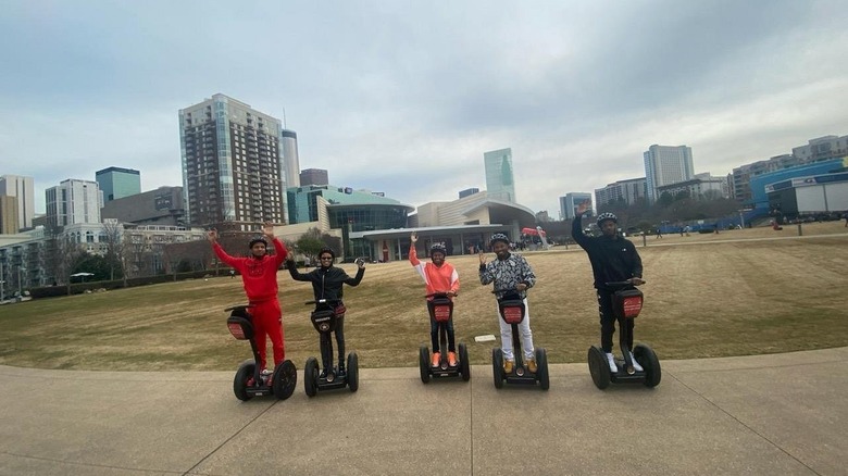 Un groupe de personnes posant et saluant sur des Segways devant les immeubles de la ville.